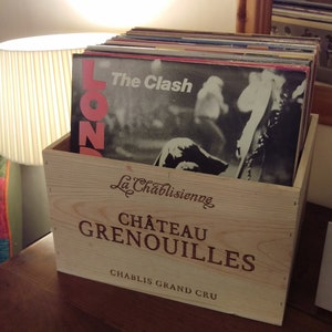 Pu&ograve; includere: Una cassa di legno con il testo "La Chablisienne Ch&acirc;teau Grenouilles Chablis Grand Cru" sul davanti. La cassa &egrave; piena di dischi in vinile, tra cui uno con il testo "The Clash" sulla copertina.