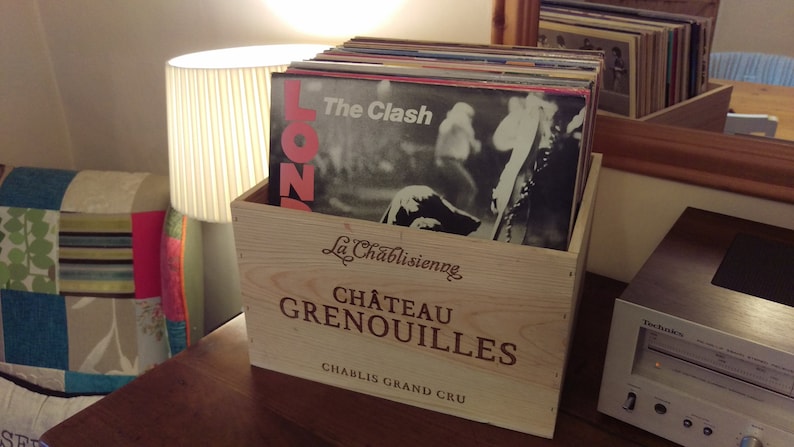 Pu&ograve; includere: Una cassa di legno con il testo "La Chablisienne Ch&acirc;teau Grenouilles Chablis Grand Cru" sul davanti. La cassa &egrave; piena di dischi in vinile, tra cui uno con il testo "The Clash" sulla copertina.