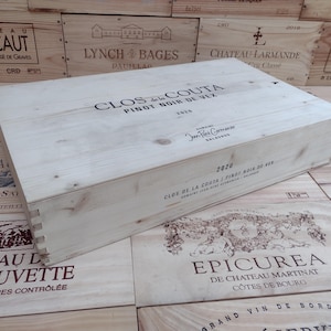 Puede incluir: Caja de vino de madera clara con la inscripción "CLOS de la COUTA PINOT NOIR DE VEX 2020". La caja está colocada sobre otras cajas de vino de madera. El texto es negro.