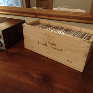 May include: A wooden wine crate with the label "Château Léoville Poyferré" and the year "2018" printed on it. The crate is filled with CDs.