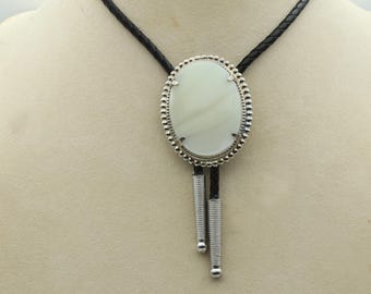 May include: A silver bolo tie with a white oval stone set in a beaded frame. The tie has a black leather cord and silver tips.