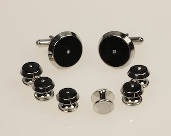May include: A set of cufflinks and collar stays with black and silver accents. Each piece features a small, clear rhinestone in the center.