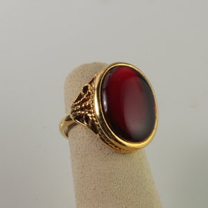 May include: A gold ring with a large, oval-shaped, red gemstone.