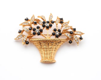May include: A gold-tone brooch featuring a basket overflowing with black and white rhinestone flowers.