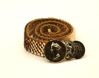 May include: A gold-colored belt made of small, overlapping metal scales. The belt has three large, round, gold-colored coin-shaped buckles.