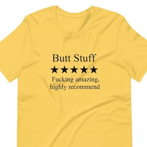 Può includere: T-shirt giallo senape con la scritta "Butt Stuff" sopra cinque stelle nere. Sotto, il testo recita "Fucking amazing, highly recommend."