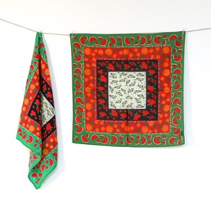 Puede incluir: Un pañuelo de tela con estampado verde, rojo y naranja con el texto "From the river to the sea" repetido en el borde.