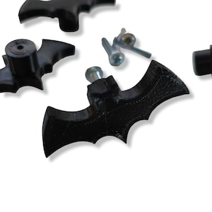 Könnte beinhalten: Drei schwarze, plastikförmige Fledermaus-Schubladenknöpfe mit silbernen Schrauben.