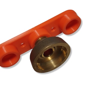 Op de afbeelding: Een oranje plastic component met twee schroefdraadopeningen en een centrale messing fitting. De messing fitting heeft een conische vorm. De component lijkt deel uit te maken van een grotere assemblage.
