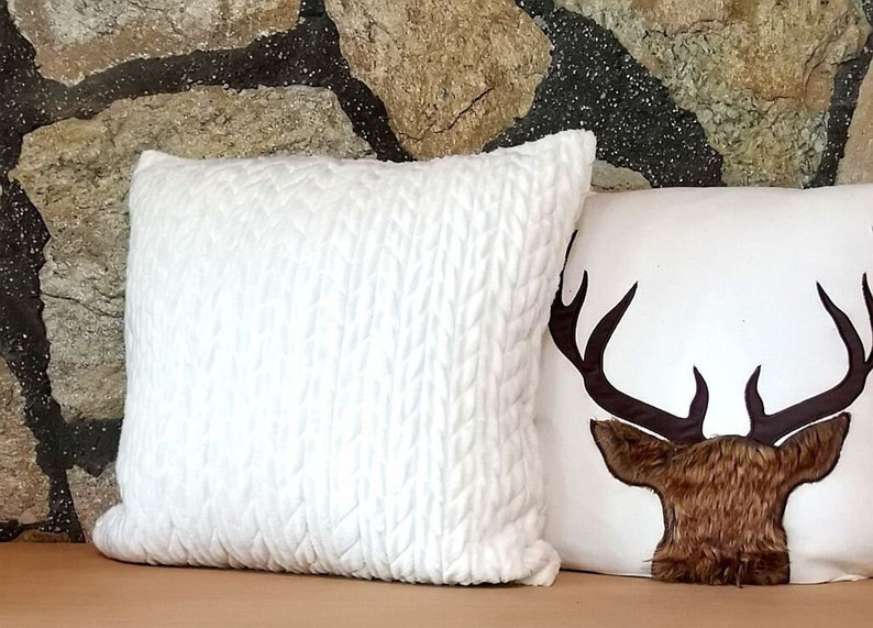 May include: Two decorative throw pillows, one white with a textured surface and one white with a brown deer head design.