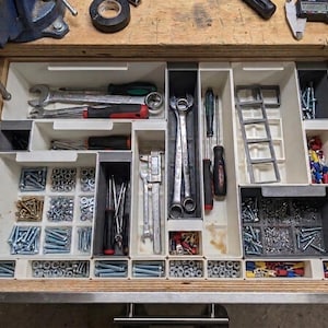 May include: A wooden drawer filled with organised tools and hardware. The drawer contains spanners, screwdrivers, a caliper, and various screws, nuts, and connectors. The tools are neatly arranged in white and grey compartments.