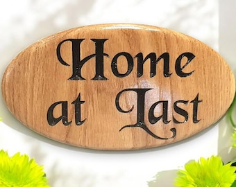 May include: A wooden oval sign with the text "Home at Last" in black lettering.
