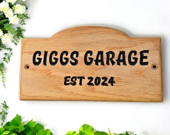 Op de afbeelding: Een houten bord met de tekst "Giggs Garage Est 2024" erin gegraveerd. Het bord is lichtbruin en heeft een licht afgeronde bovenkant.