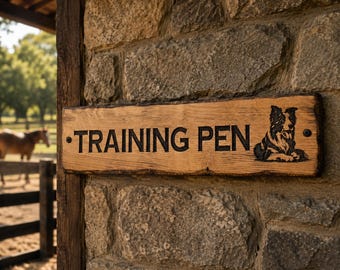 Op de afbeelding: Een rechthoekig houten bord met een natuurlijke rand, voorzien van de zwarte tekst "TRAINING PEN" en een gedetailleerde zwarte illustratie van een Border Collie. Het bord is met twee donkere metalen schroeven op een stenen muur bevestigd.