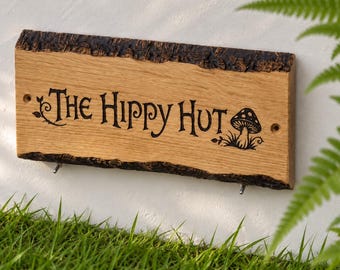 May include: A rectangular wooden sign with natural live edges and dark bark texture. The light brown wood features the engraved black text "THE HIPPY HUT" in a stylized font, accompanied by a small engraved mushroom graphic and vine details.