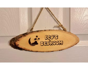 Op de afbeelding: Een houten bord met een halve maan en sterren ontwerp, de tekst "Leo's Bedroom" is in het hout gebrand.