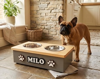 May include: A rectangular elevated pet feeder with a light wood top and a dark gray base. The base features the name MILO in white lettering flanked by two white paw print icons. Two stainless steel bowls are set into the wooden top surface.