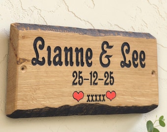 Op de afbeelding: Houten bord met de namen "Lianne & Lee" in zwart schrift. De datum "25-12-25" staat eronder, met twee rode harten en het woord "xxxxx". Het bord heeft een natuurlijke houtnerf en een donkere, ruwe rand.