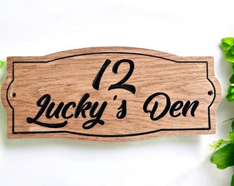 Op de afbeelding: Een houten bord met een gebogen bovenkant en zwarte letters. Het bord staat "12 Lucky's Den".