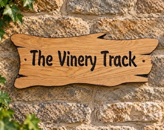May include: A rectangular wooden sign with a natural live edge, featuring the text "The Vinery Track" engraved in dark, bold lettering. The light brown wood grain is visible across the surface, and two small holes are present for mounting.