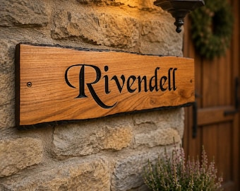 Op de afbeelding: Een rechthoekig houten bord met een natuurlijke boomrand, voorzien van het woord Rivendell in zwarte letters. Het bord is bevestigd aan een gestructureerde stenen muur met zichtbare metalen schroeven aan de linker- en rechterkant.