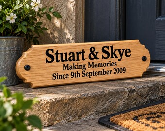 May include: A rectangular light brown wooden sign with decorative scalloped edges and two black screws. The sign features black engraved text that reads: Stuart & Skye, Making Memories, Since 9th September 2009. The wood grain is clearly visible.