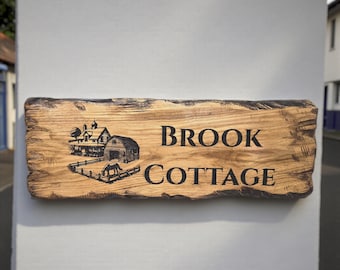 Op de afbeelding: Houten bord met de zwarte tekst "BROOK COTTAGE". Het bord toont een gedetailleerde illustratie van een huis, schuur en een paard in een omheining. Het hout heeft een natuurlijke nerf.