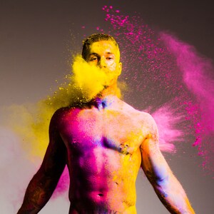 Puede incluir: Un hombre cubierto de polvo rosa y amarillo, con una nube de polvo amarillo frente a su cara.