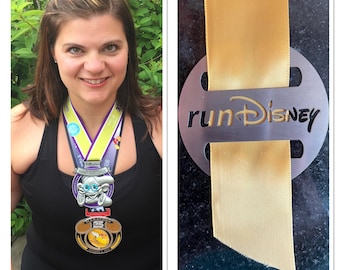 Puede incluir: Una mujer con un top negro sin mangas y una medalla de color morado, amarillo y azul alrededor del cuello. La medalla tiene una figura de Mickey Mouse plateada. La medalla está unida a una cinta amarilla con las palabras "runDisney" en ella.