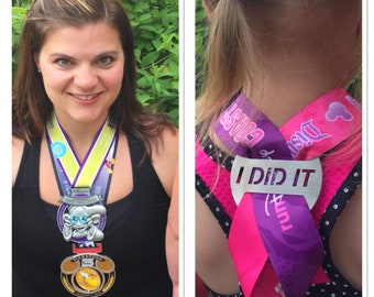 Puede incluir: Dos personas con medallas y una cinta morada con el texto "I Did It" y las palabras "Disney Coast to Coast" en ella. La cinta está atada alrededor del cuello de la persona en el lado derecho de la imagen.