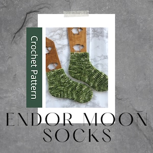 May include: A pair of green and white crochet socks displayed on a wooden sock block. The socks are a textured stitch and have a subtle ombre effect. The text "Endor Moon Socks" is displayed below the image.