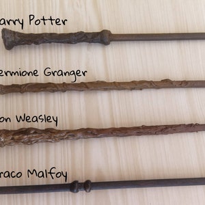 Puede incluir: Se muestran cuatro varitas de la serie Harry Potter. Las varitas est&aacute;n etiquetadas con los nombres "Harry Potter", "Hermione Granger", "Ron Weasley" y "Draco Malfoy". Cada varita tiene un dise&ntilde;o y color &uacute;nicos, que van del marr&oacute;n oscuro al negro.