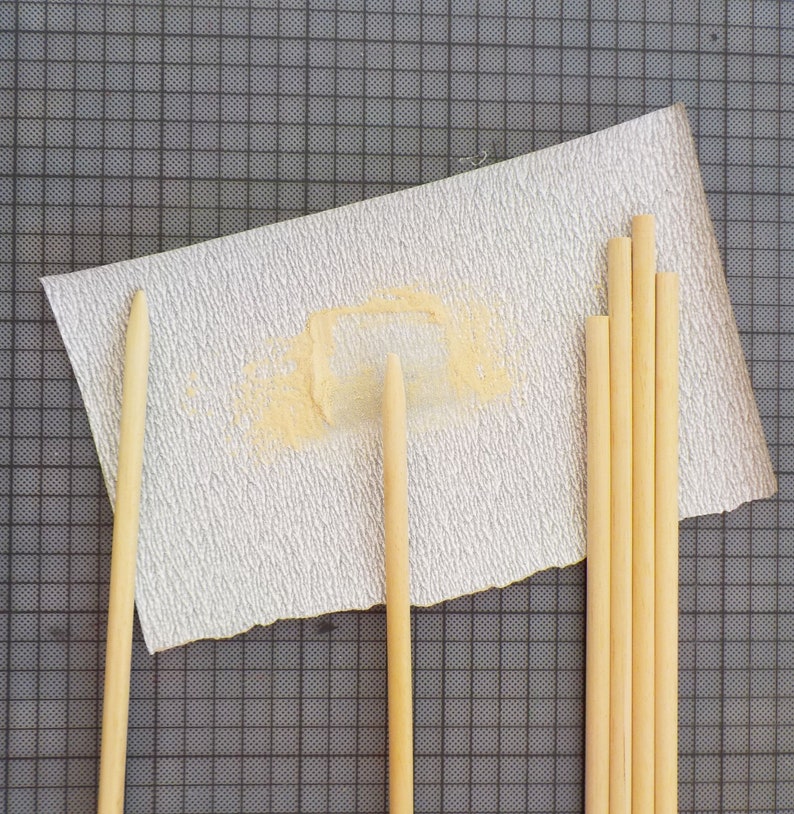 Puede incluir: Un surtido de espigas de madera de color marr&oacute;n claro y un trozo de papel de lija. El papel de lija es blanco con una superficie texturizada y una mancha amarilla clara. Las espigas son de diferentes longitudes y est&aacute;n dispuestas cerca del papel de lija.