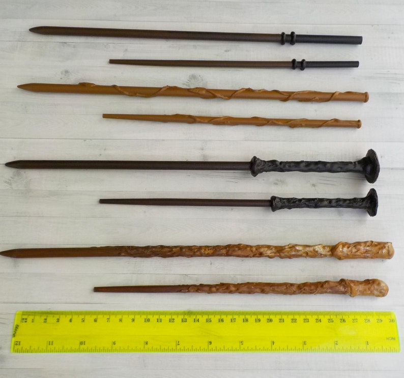 Puede incluir: Variedad de varitas de madera en tonos marrones, desde oscuros hasta claros. Algunas varitas tienen empu&ntilde;aduras texturizadas o elementos decorativos. Una regla amarilla en la parte inferior muestra medidas en cent&iacute;metros.