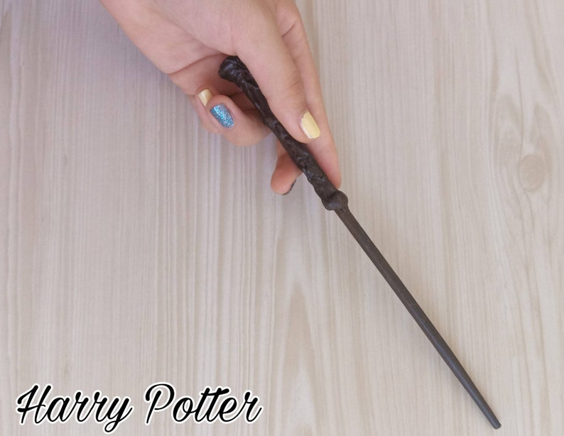 Puede incluir: Una varita marr&oacute;n oscuro con detalles intrincados, sostenida sobre una superficie clara de vetas de madera. La varita es delgada y parece ser de madera. El texto "Harry Potter" est&aacute; en la parte inferior de la imagen.