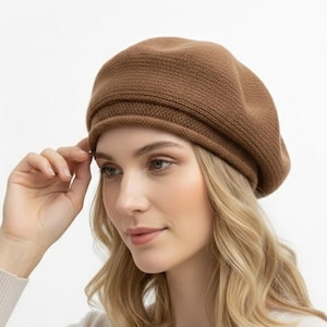 Op de afbeelding: Een bruine gebreide baret. De baret is effen van kleur en heeft een geribbelde rand. De baret is gemaakt van een zacht, getextureerd materiaal. De baret is een klassieke stijl en kan met een verscheidenheid aan outfits worden gedragen.