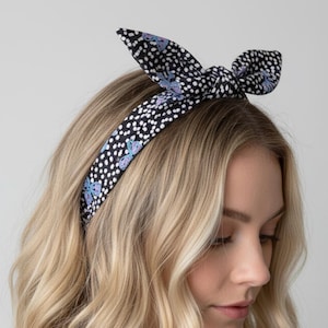 May include: A black and white polka dot headband with a bow. The headband has small white dots on a black background, with a repeating pattern of purple and blue butterflies. The bow is tied at the top of the head.