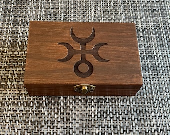 May include: A wooden box with a latch and a carved symbol on the lid. The symbol is a circle with three crescent moons around it.
