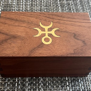 May include: A wooden box with a gold inlay of a geometric design. The box is made of dark wood with a natural grain.