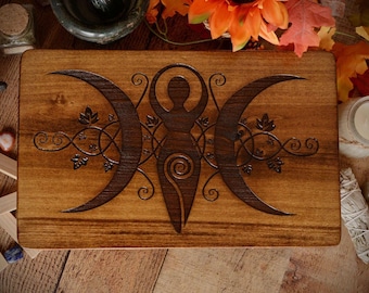 May include: A rectangular wooden box featuring a dark brown laser-engraved design on its lid. The central motif depicts a stylized female figure with a spiral at the abdomen, flanked by two crescent moons and intricate vine and leaf patterns.