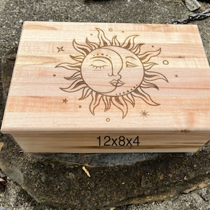 May include: A wooden box with a sun and moon design engraved on the lid. The box is 12 inches by 8 inches by 4 inches.