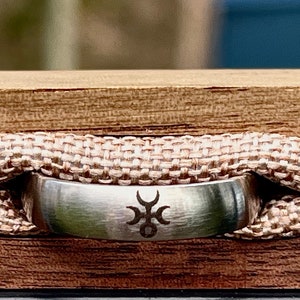 May include: A silver ring with a geometric design is displayed in a wooden box lined with beige fabric.