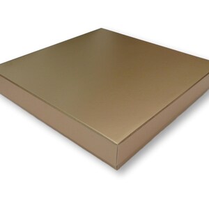 Puede incluir: Una caja de cartón de color dorado con una parte superior lisa y plana. La caja está cerrada y parece estar vacía.