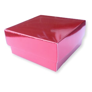 Puede incluir: Una caja de regalo cuadrada de color rojo brillante. La caja está hecha de cartón y tiene un acabado liso y brillante.