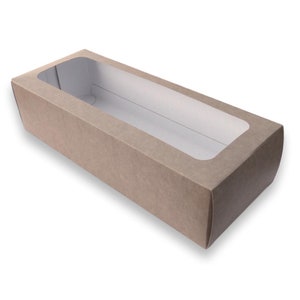 Puede incluir: Una caja de cartón marrón con una ventana transparente, diseñada para empaquetar y exhibir productos.