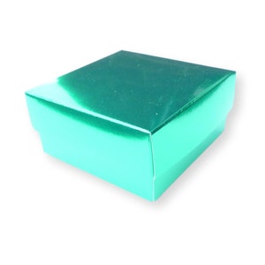 Puede incluir: Una caja de regalo cuadrada de color verde azulado con un acabado brillante. La caja tiene tapa y base, y está sobre un fondo blanco. La caja está vacía y lista para ser llenada con un regalo.