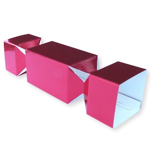 Puede incluir: Un petardo navideño de color rosa brillante con brillo metálico. El petardo tiene una sección central rectangular y extremos cuadrados, con detalles blancos en los pliegues. La decoración festiva está sobre un fondo blanco.