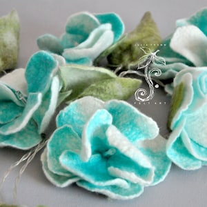 May include: A garland of felt flowers in shades of turquoise and white, with green felt leaves. The handmade floral arrangement features multiple blossoms and leaves, strung together with a thin wire. The flowers have a soft, textured appearance.