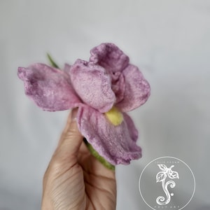 May include: A hand holds a purple felt flower with a yellow centre. The flower is made of wool and has a realistic appearance.