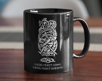 May include: Black ceramic mug with a white design of a warrior holding a sword and shield, surrounded by a dragon and runes. The runes read: "SRIXS:FBRNT:XRØNS: SRIXS:FBRNT:HMRRMS:"